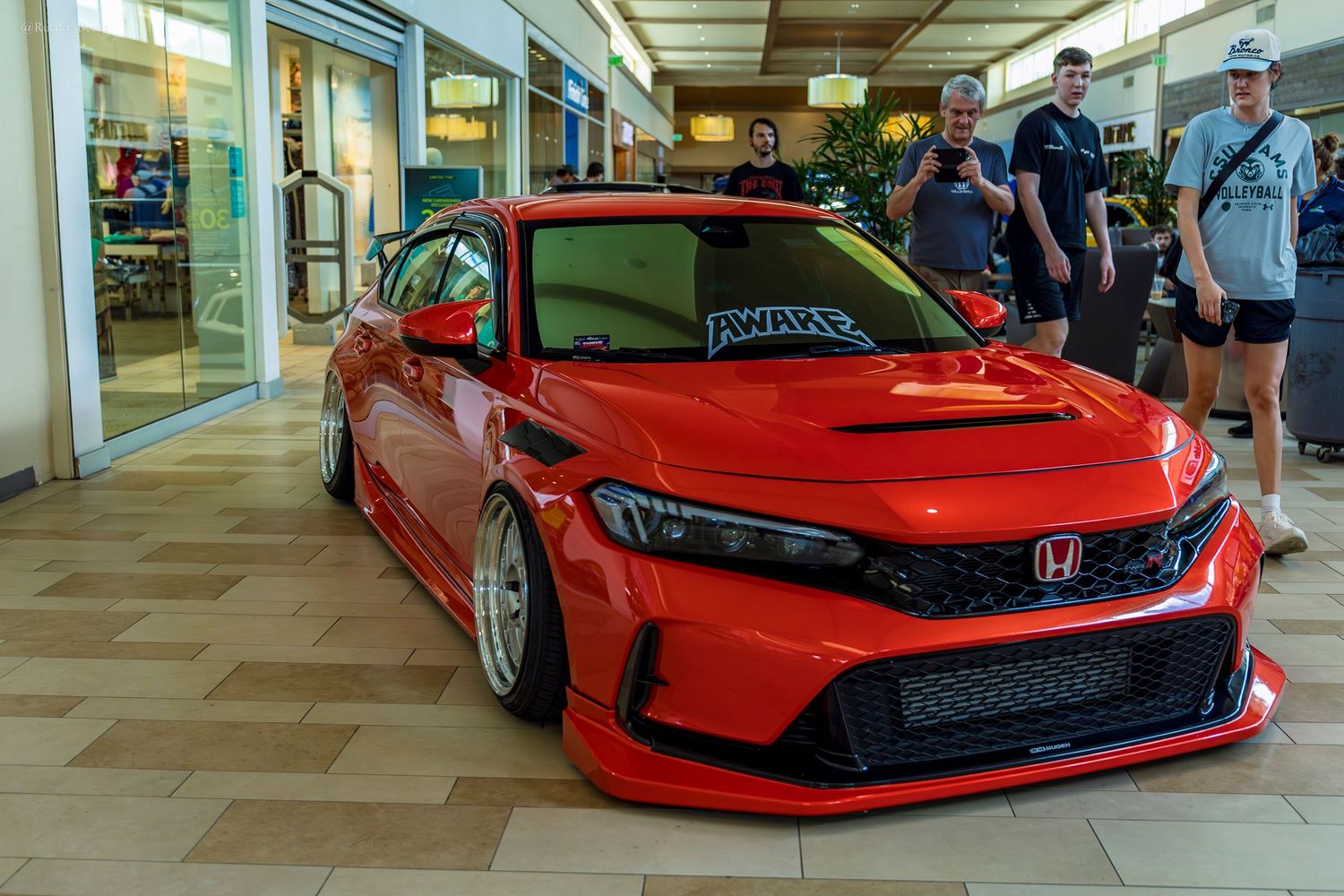 Red Honda Civic hatchback with wide body kit and custom front bumper at car meet.