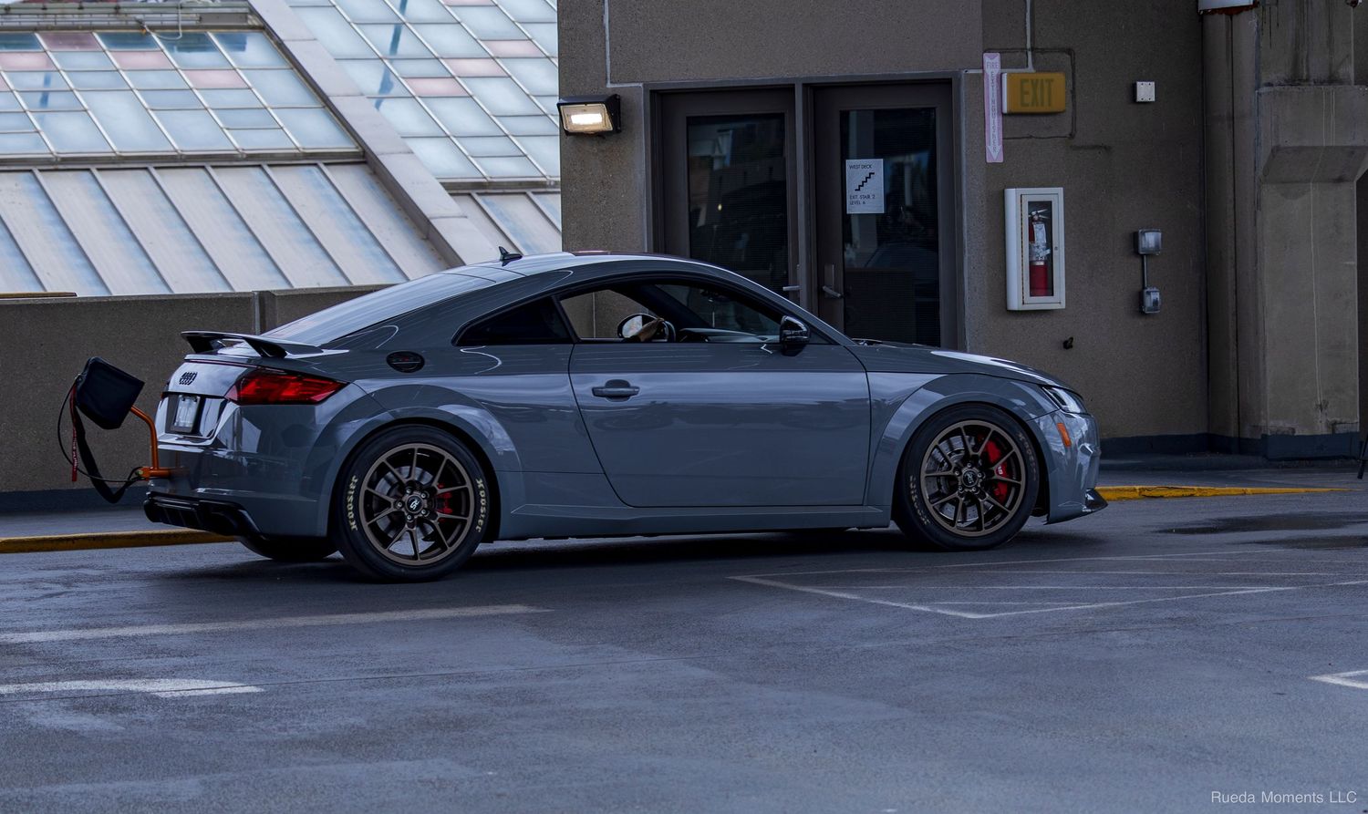 Gray Audi TT RS with large rear spoiler and red brake calipers parked at a car meet.