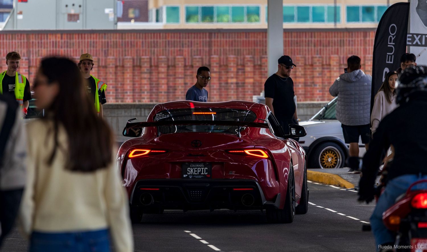Rear view of a red Toyota Supra with glowing taillights at an outdoor automotive event.