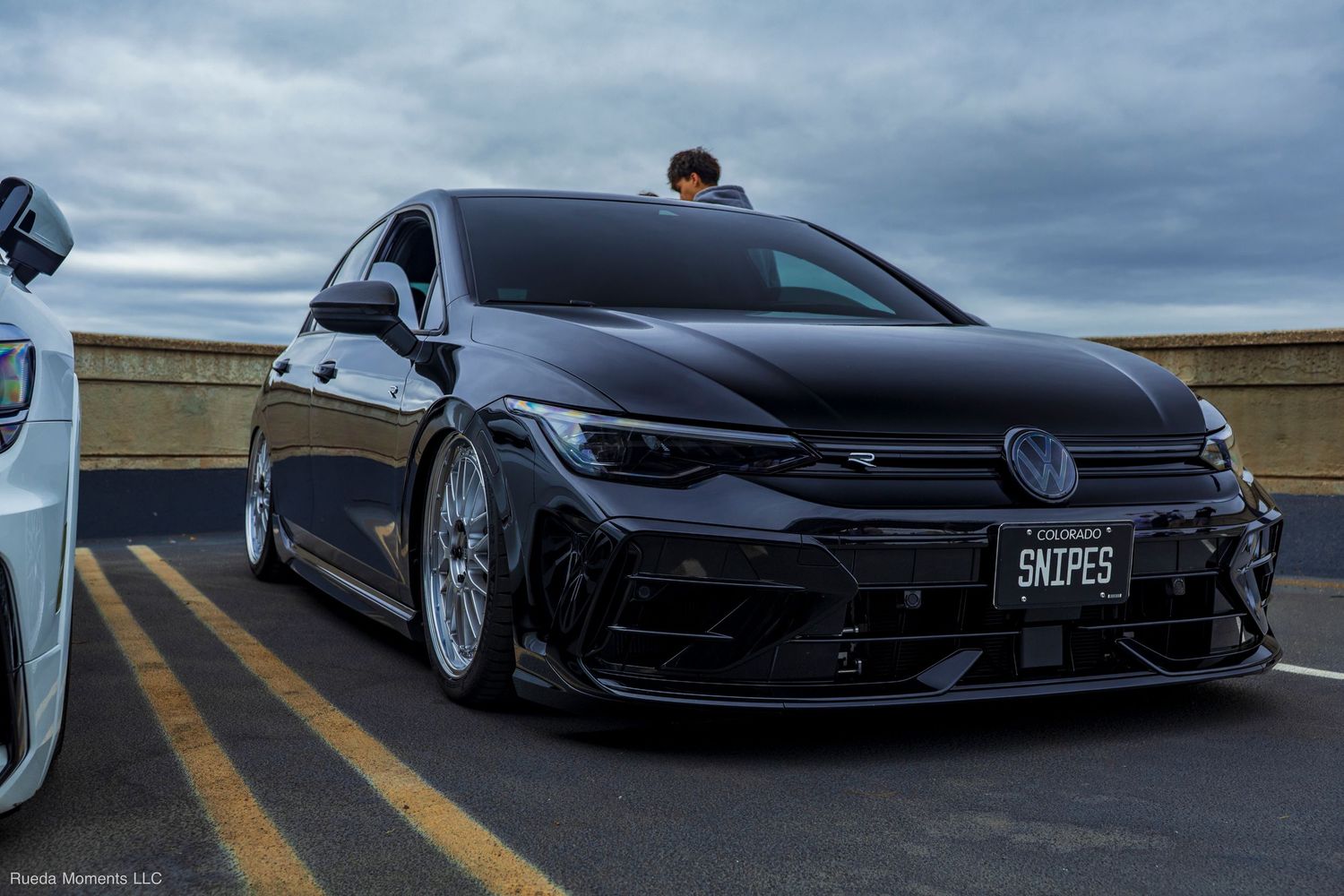 Slammed black Volkswagen Golf R with custom license plate SNIPES at a rooftop car meet.