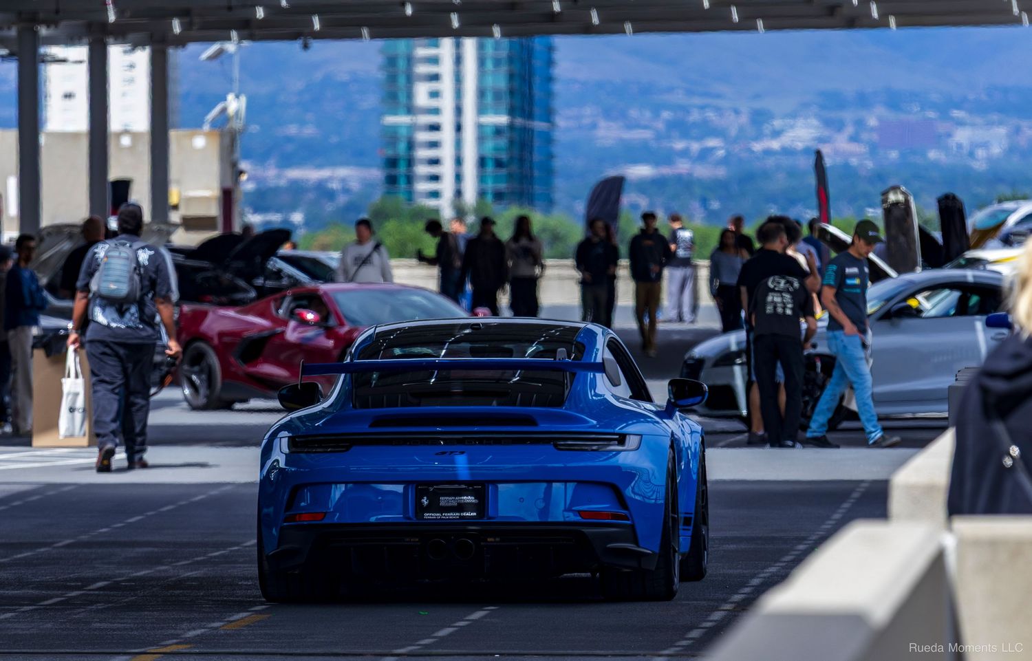 Blue Porsche 911 GT3 RS rear view at an outdoor car show with city skyline visible.