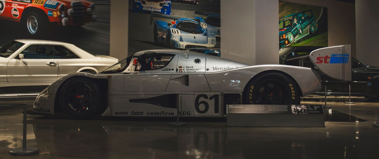 Silver Le Mans prototype race car number 61 on display in a motorsport museum.