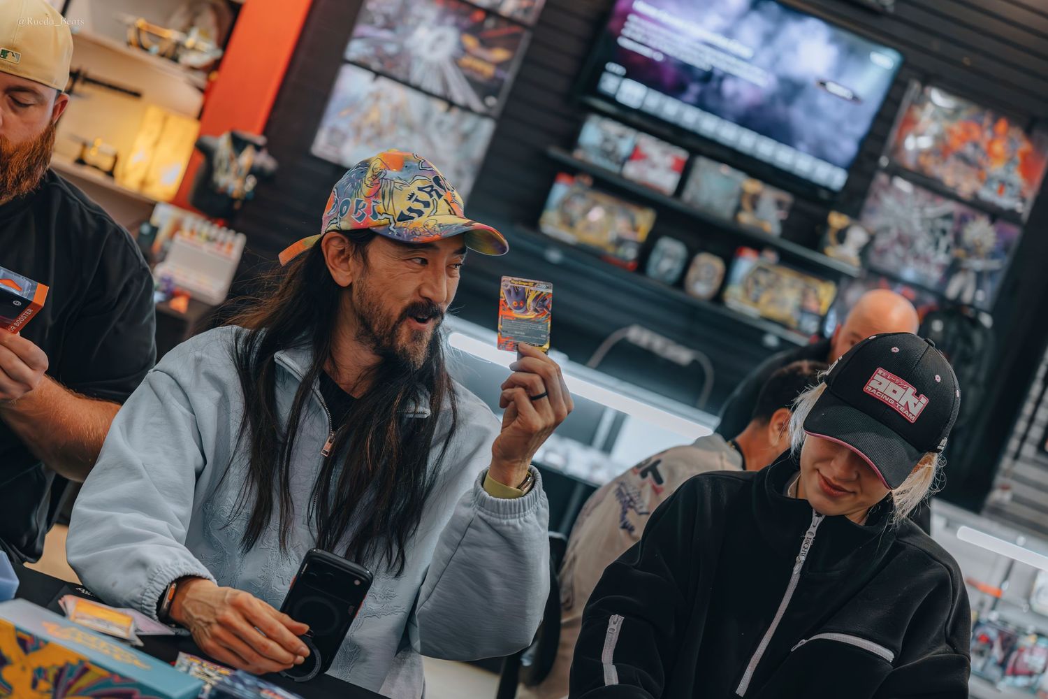 Man with long hair and colorful cap holds trading card at collector event.