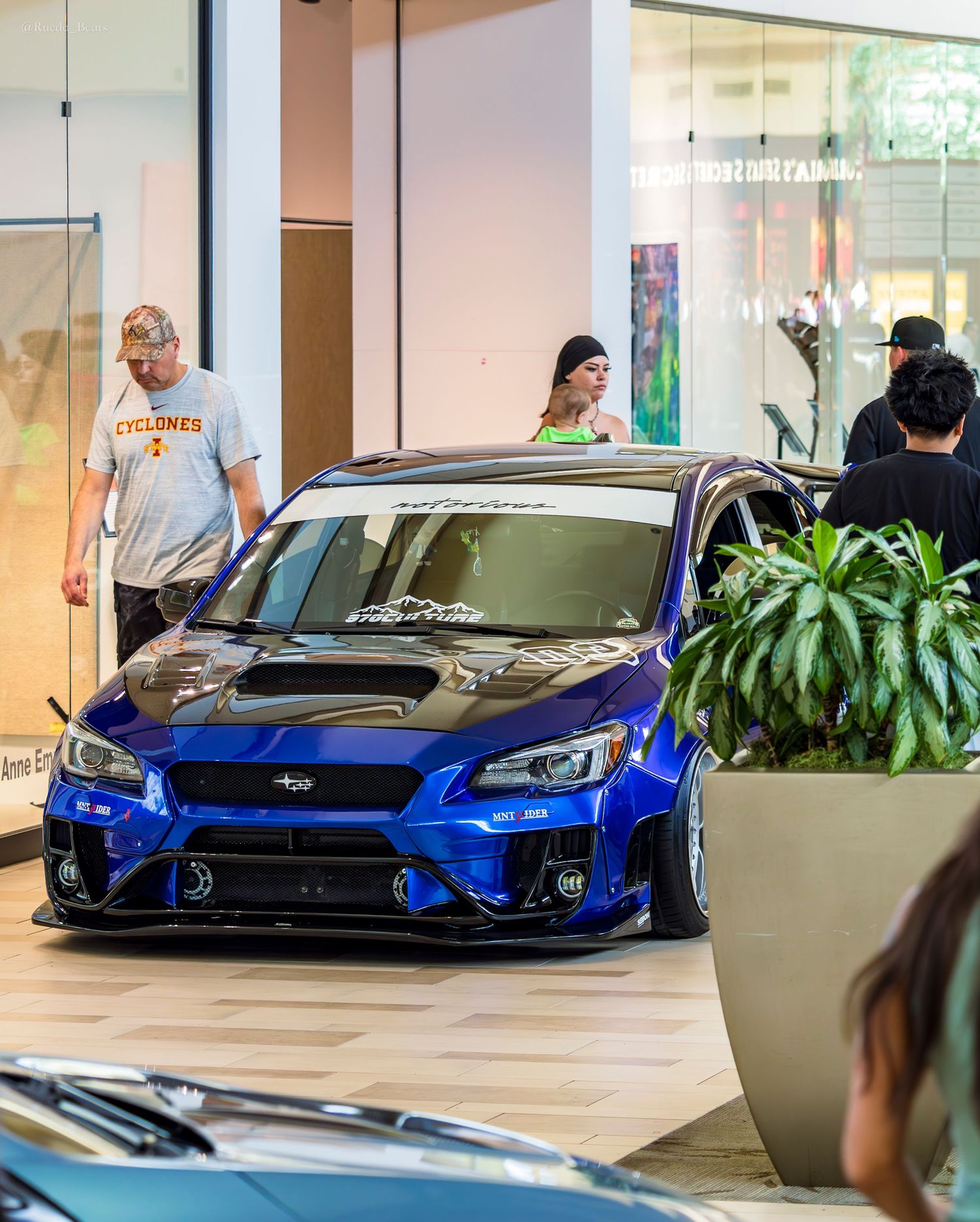 Widebody bagged blue Subaru WRX STI on display at an indoor automotive car show event.