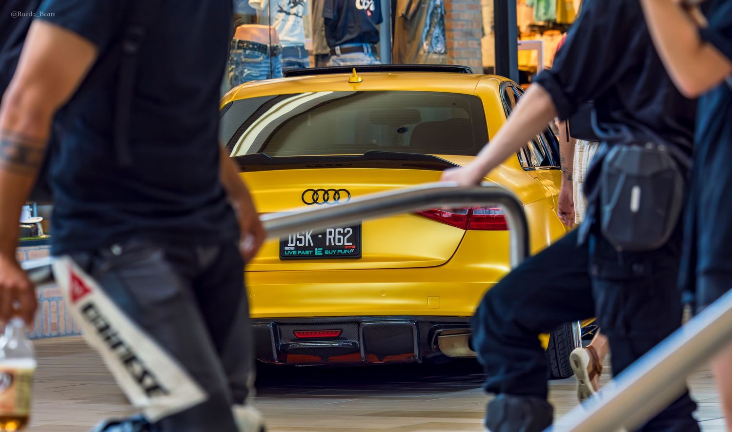 Yellow Audi sports car with green license plate JSK R62 parked inside busy shopping mall car show.