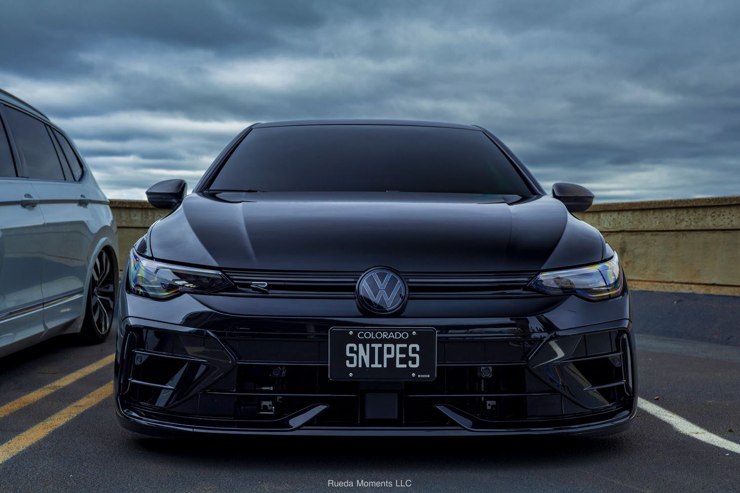 Aggressive front end of a black Volkswagen Golf R with SNIPES Colorado license plate at a car meet.