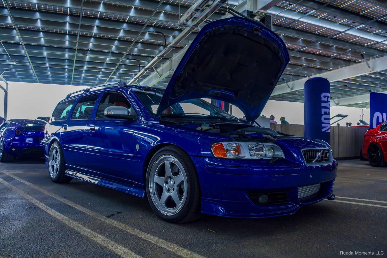 Blue Volvo V70 R wagon with hood open on display at an outdoor car show.