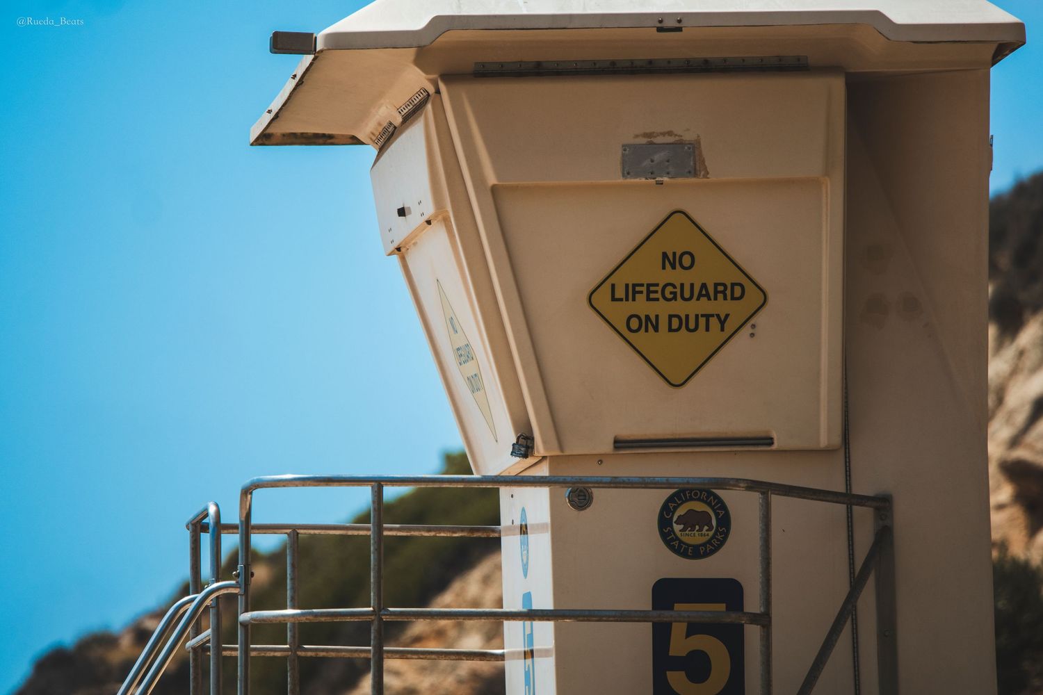 Lifeguard tower station number 5 with No Lifeguard On Duty warning sign against a clear blue sky.