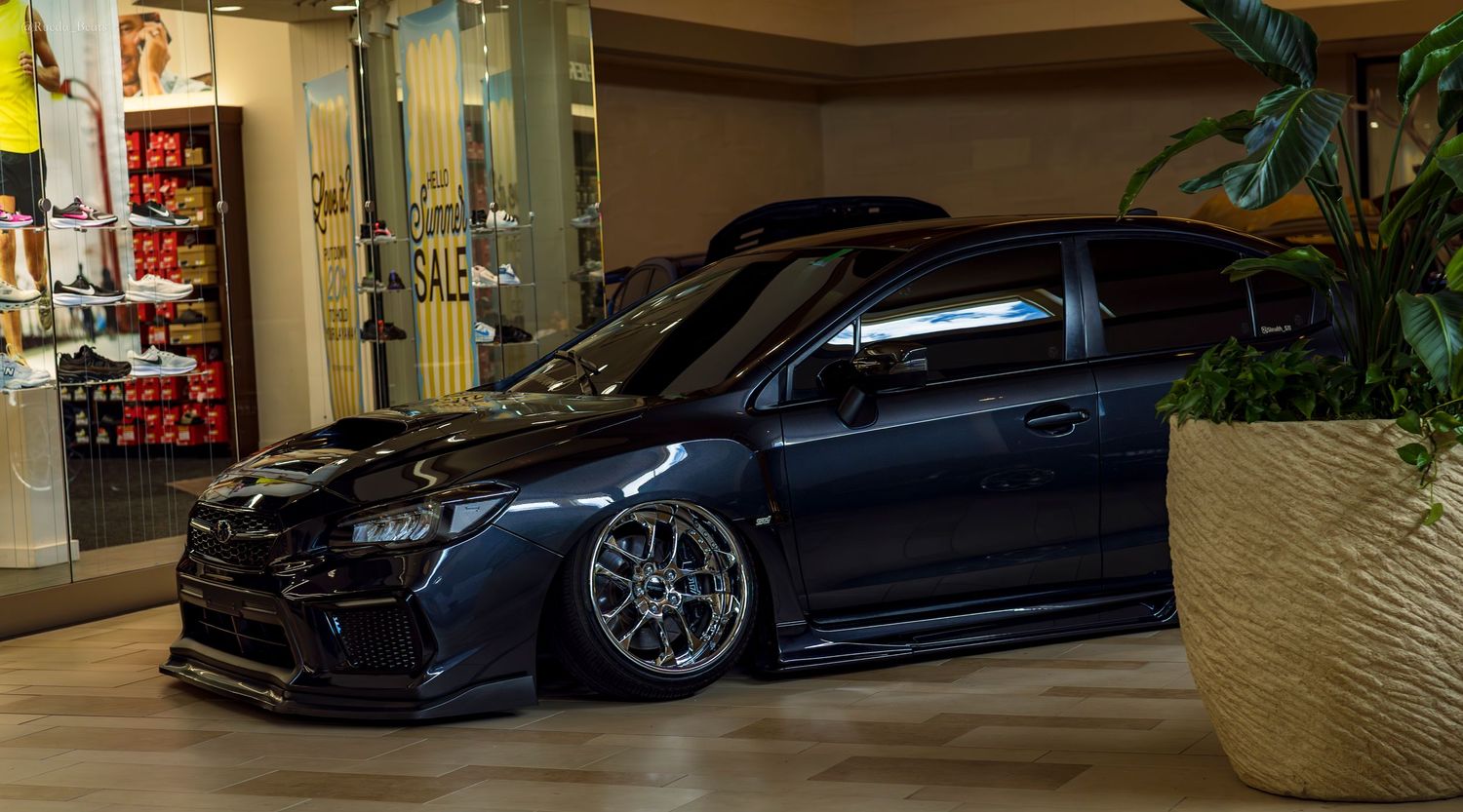 Blacked-out Mitsubishi Lancer Evo widebody stanced at an indoor mall car show.
