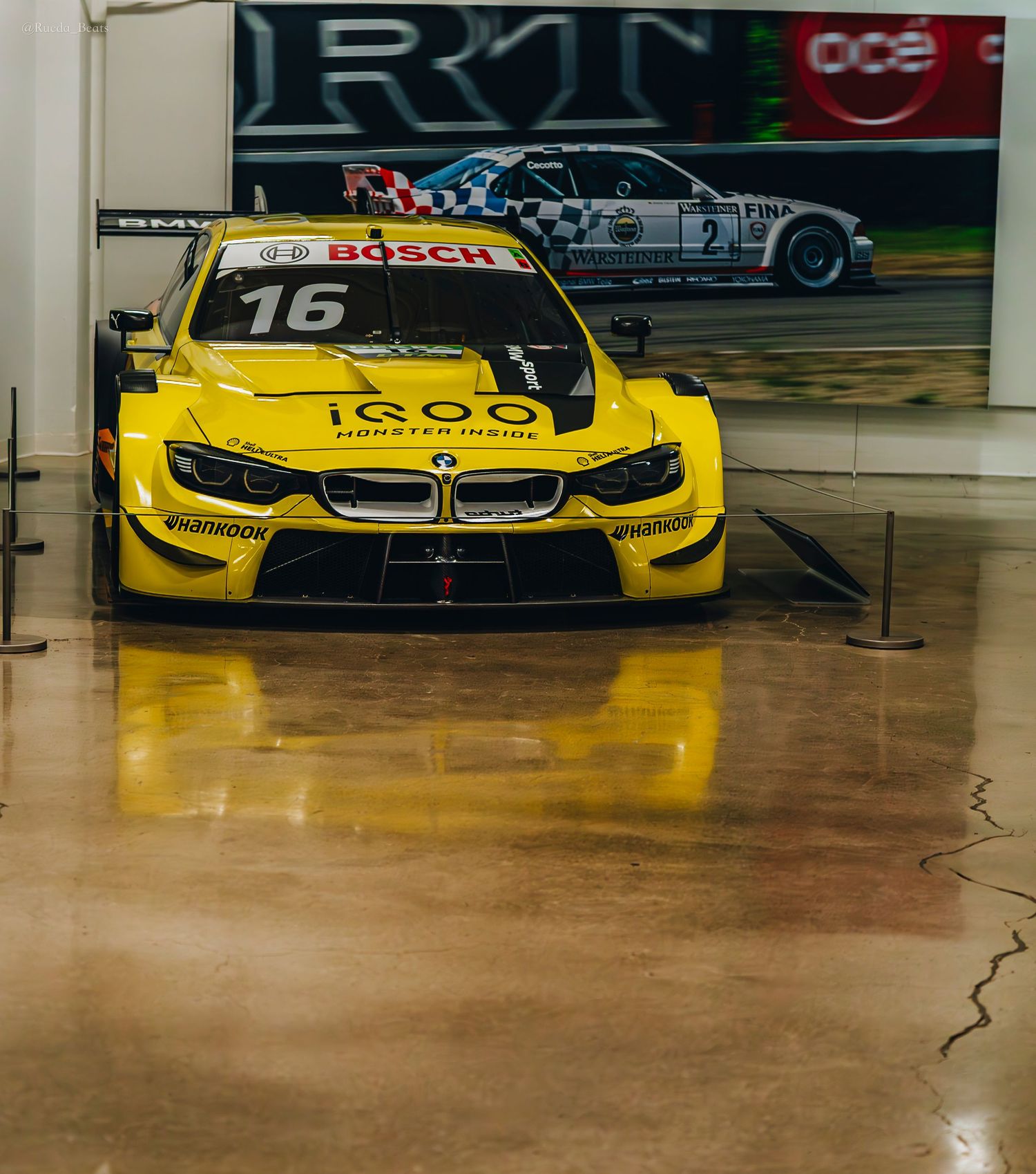 Yellow BMW M4 DTM race car number 16 with iQOO sponsorship at an indoor exhibit.
