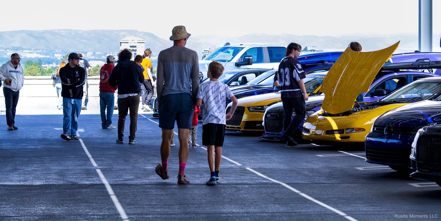 Adult and child walking hand in hand past colorful exotic cars at an outdoor car show.