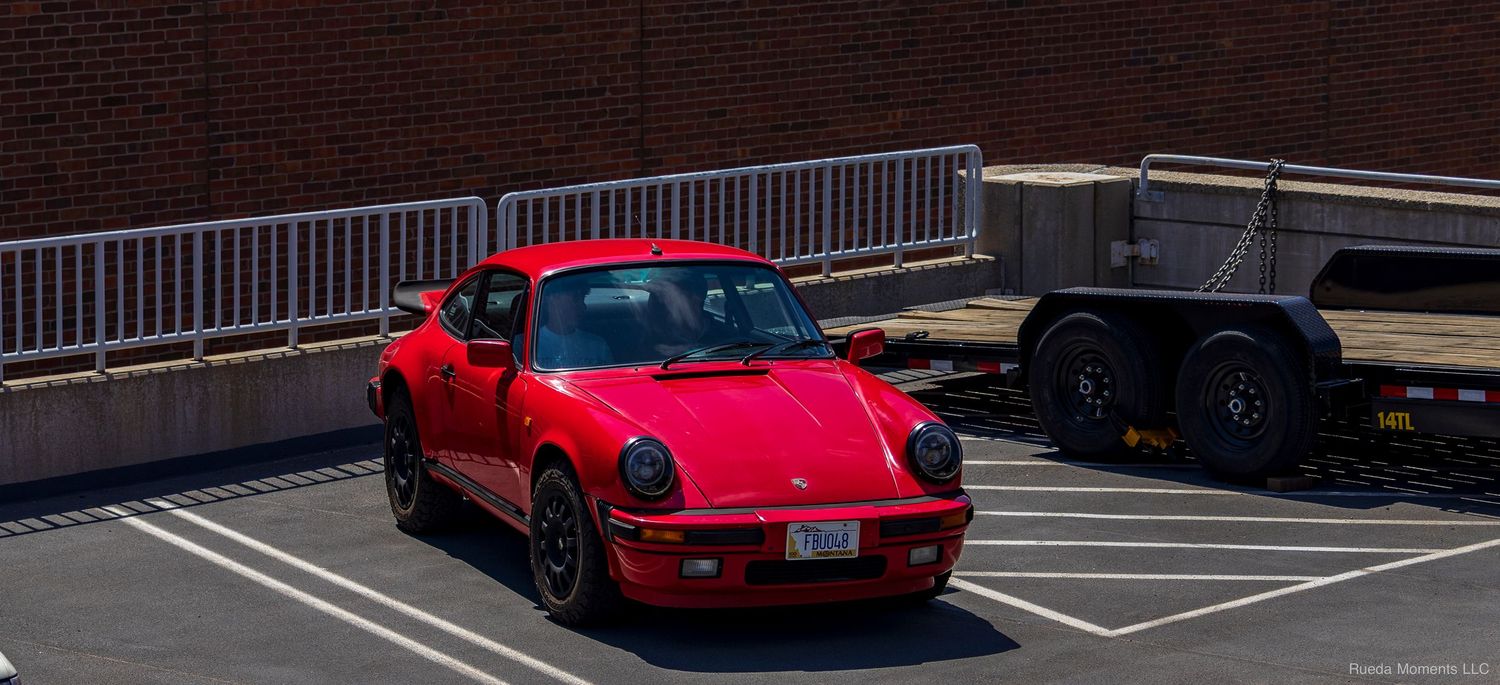 Classic red Porsche 911 parked in a sunny lot next to a utility trailer.