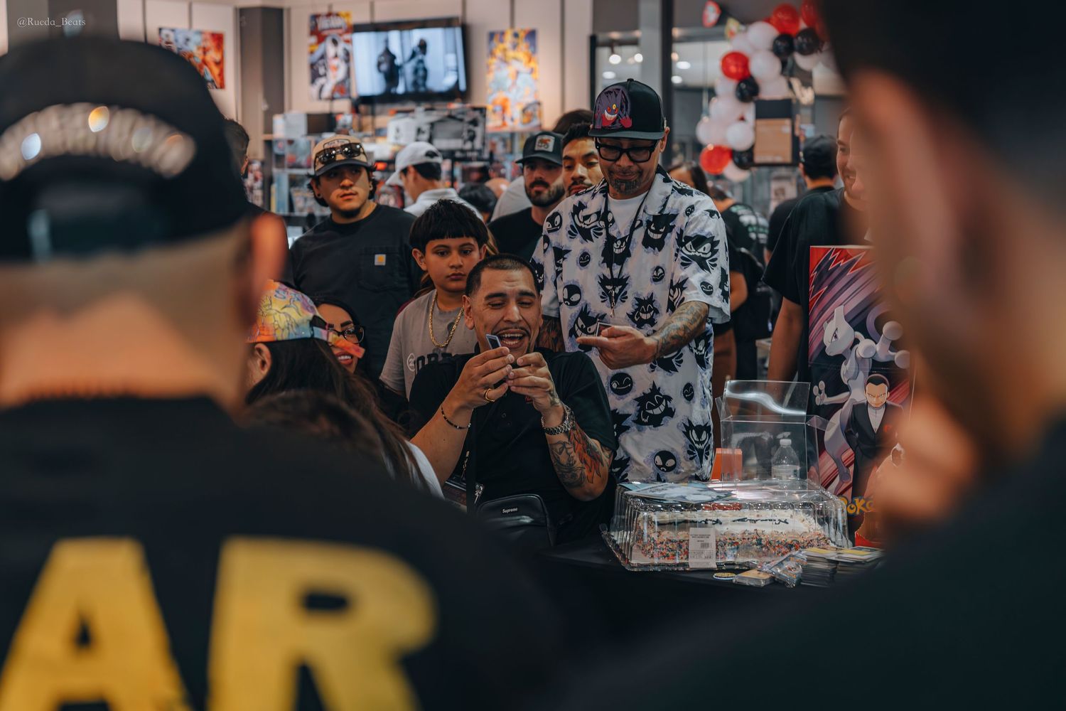 Group of men gathered around a display case at an indoor trading card event.