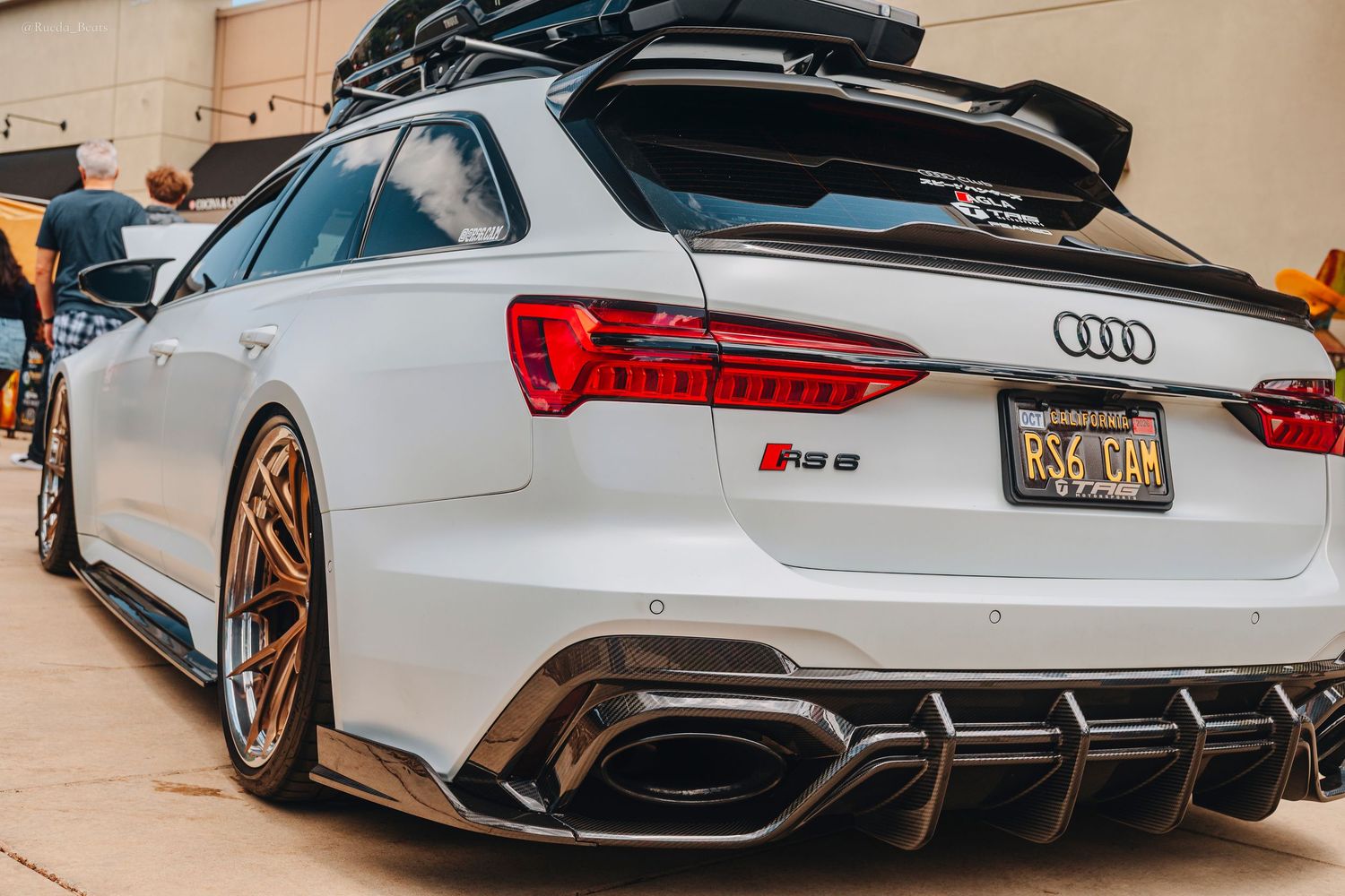 White Audi RS6 Avant with gold wheels and carbon diffuser at car show.