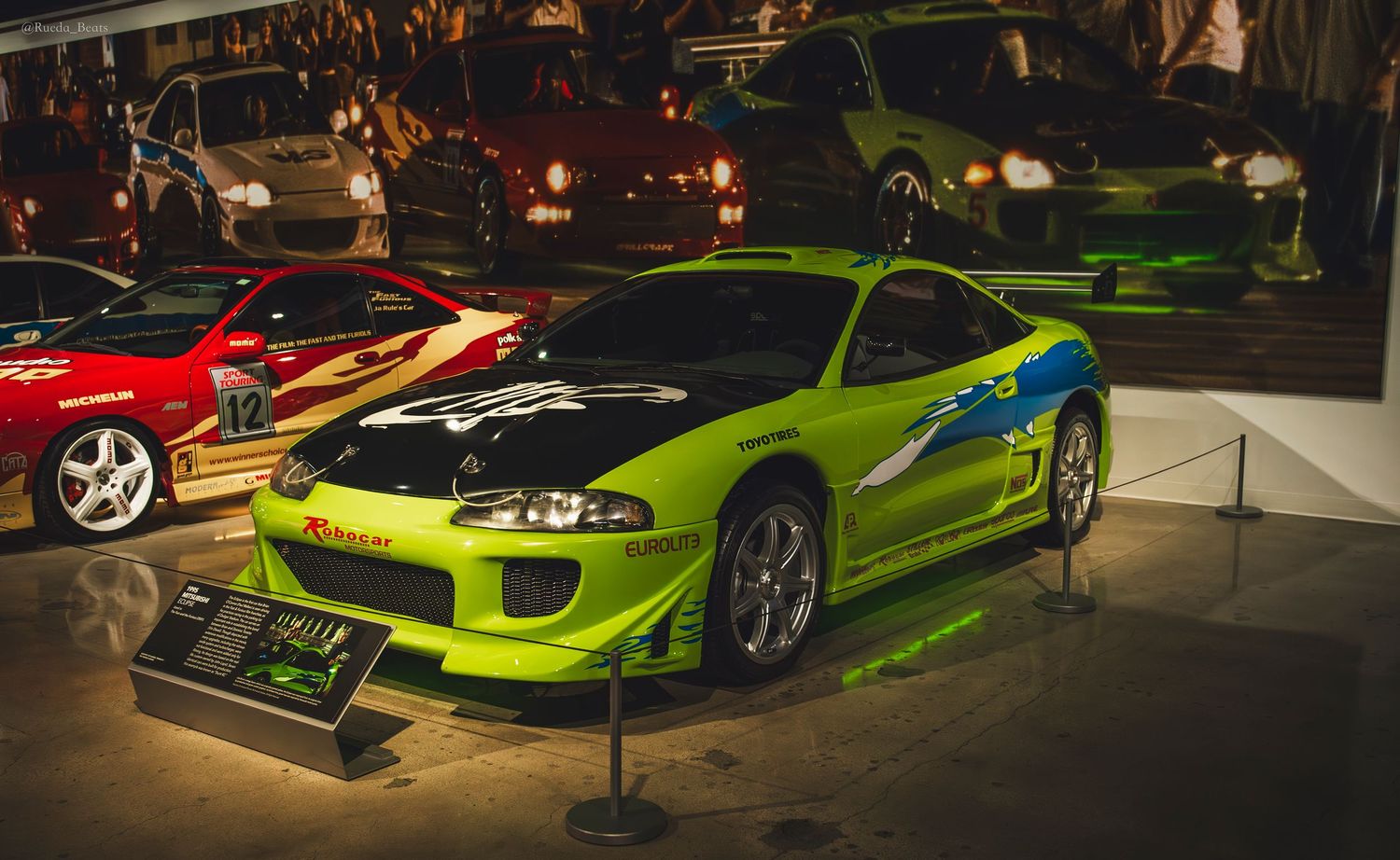 Green Mitsubishi Eclipse with custom graphics on display at Fast and Furious movie car museum exhibit.