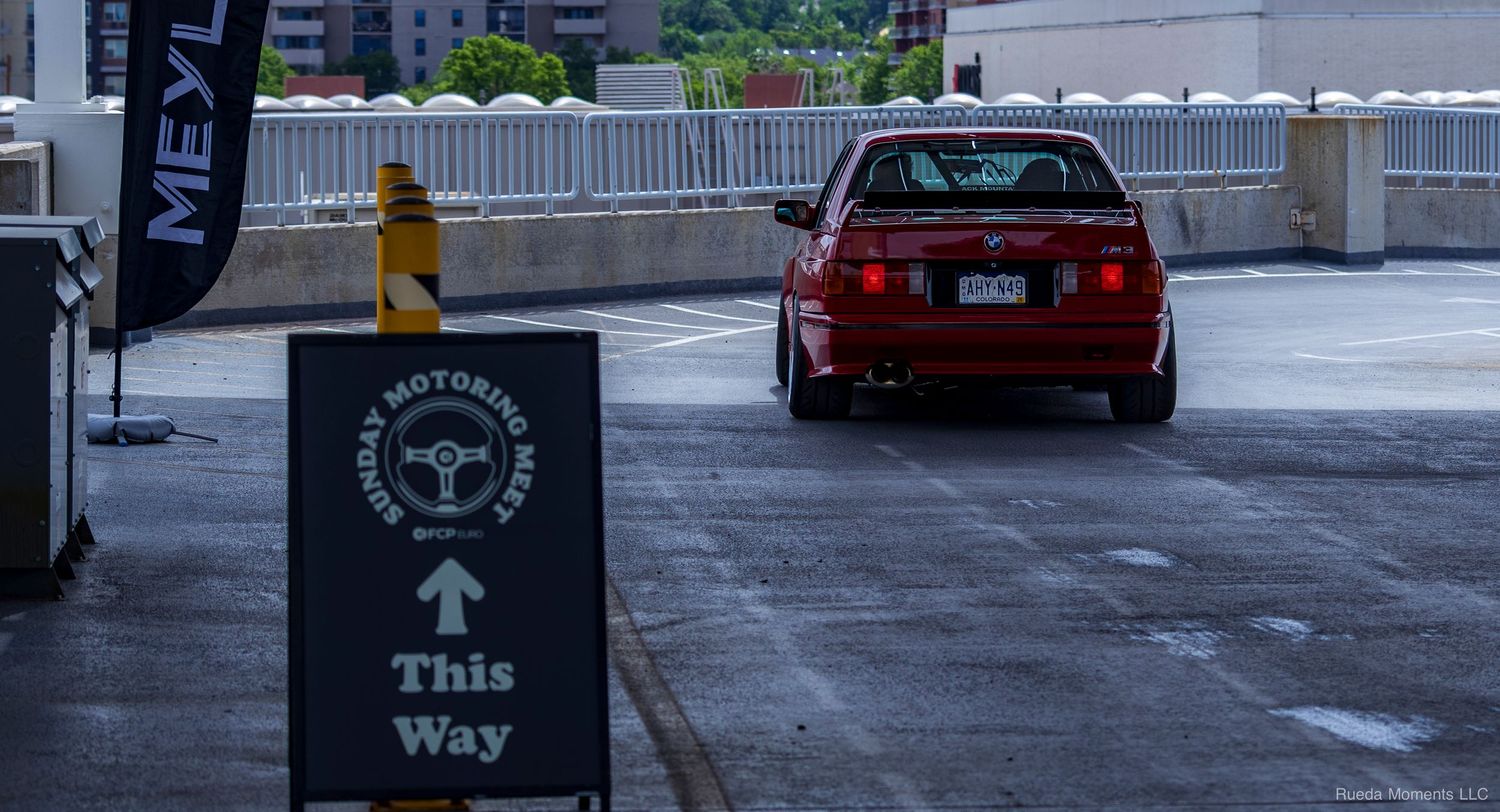 Red BMW sedan parked near a Berkeley Motoring Club This Way sign in a parking garage.