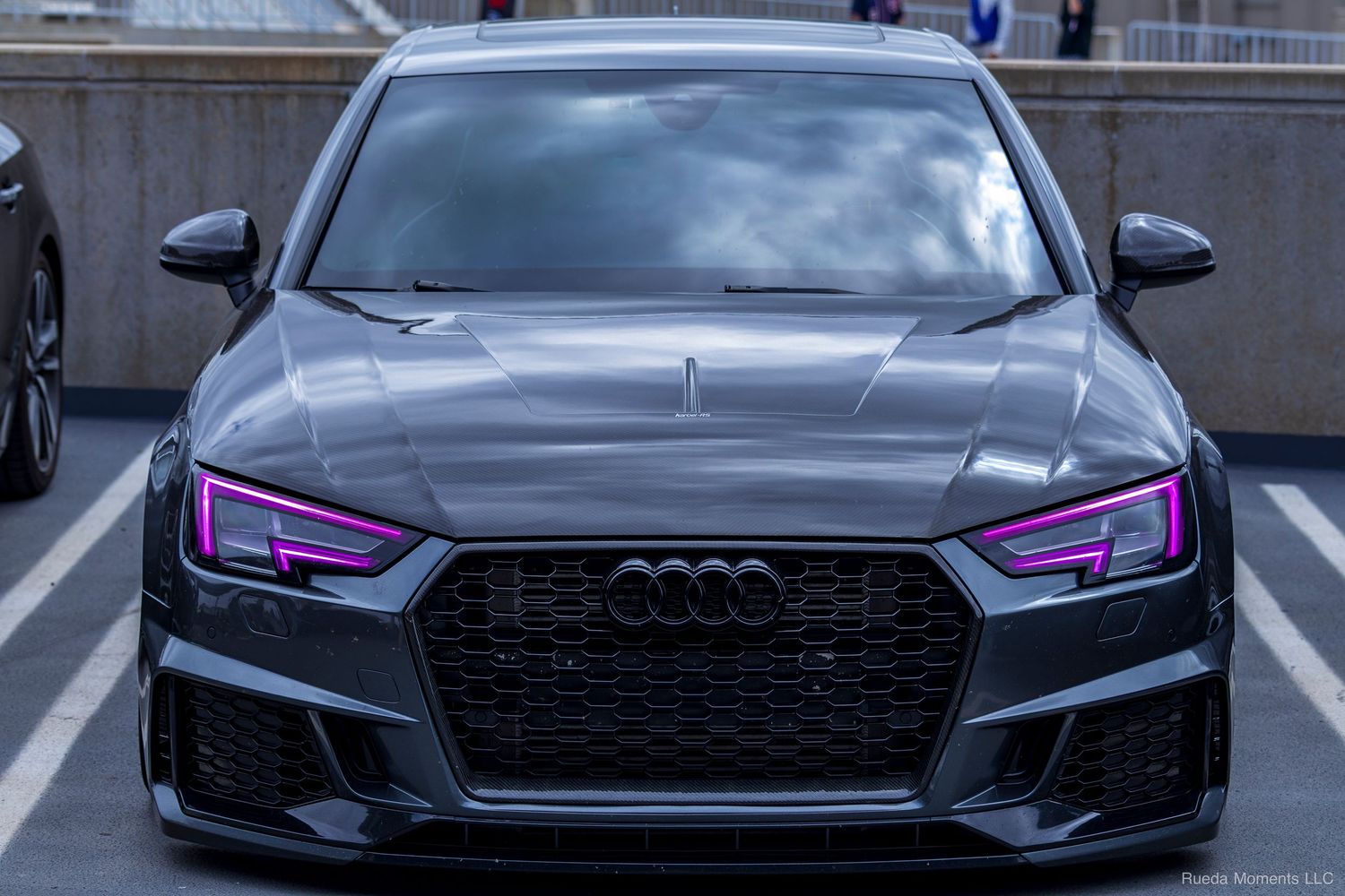 Gray Audi RS4 front view with pink LED headlights in a parking garage at a car meet.