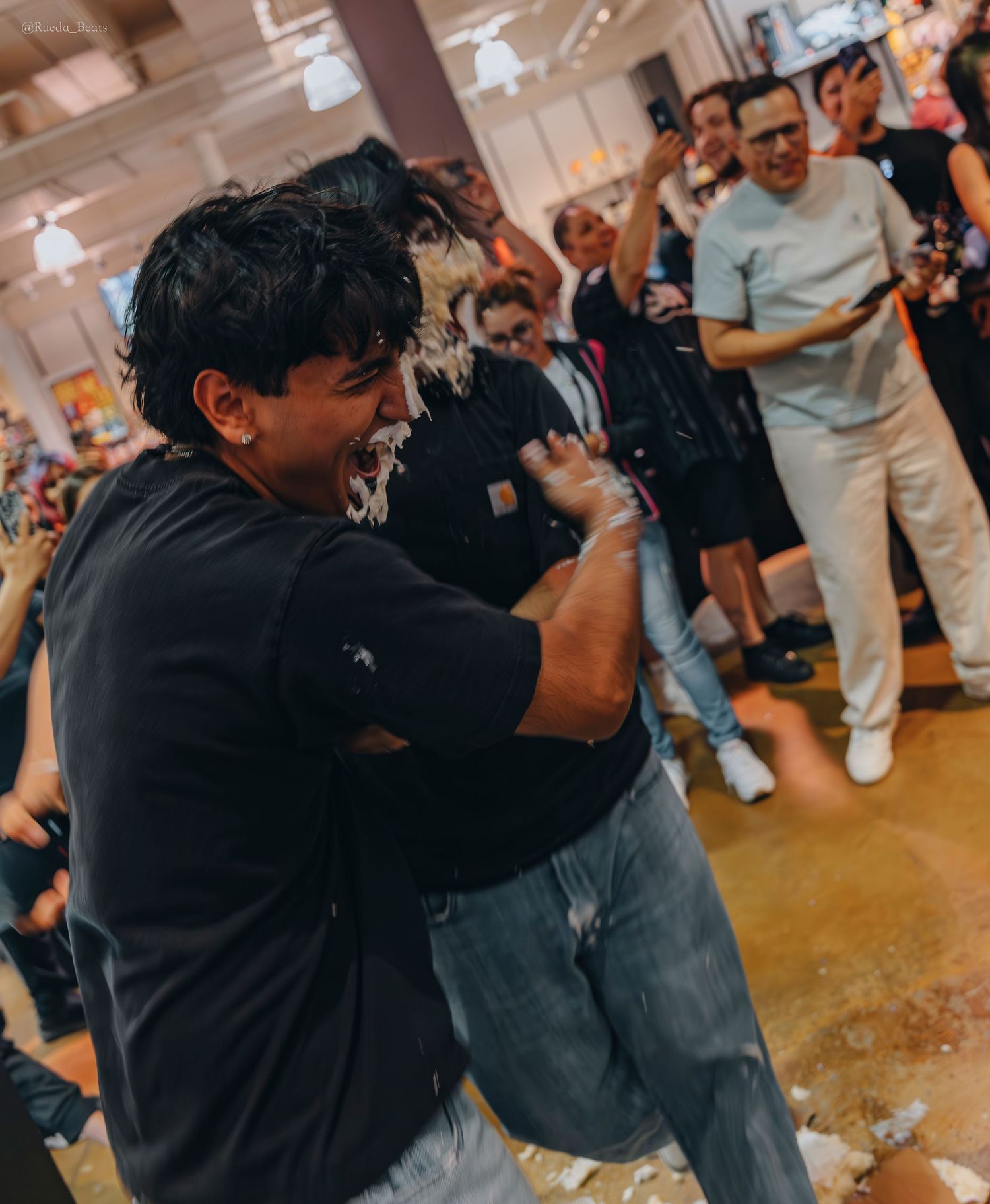 Two people with cake smashed on their faces laughing at a lively party.