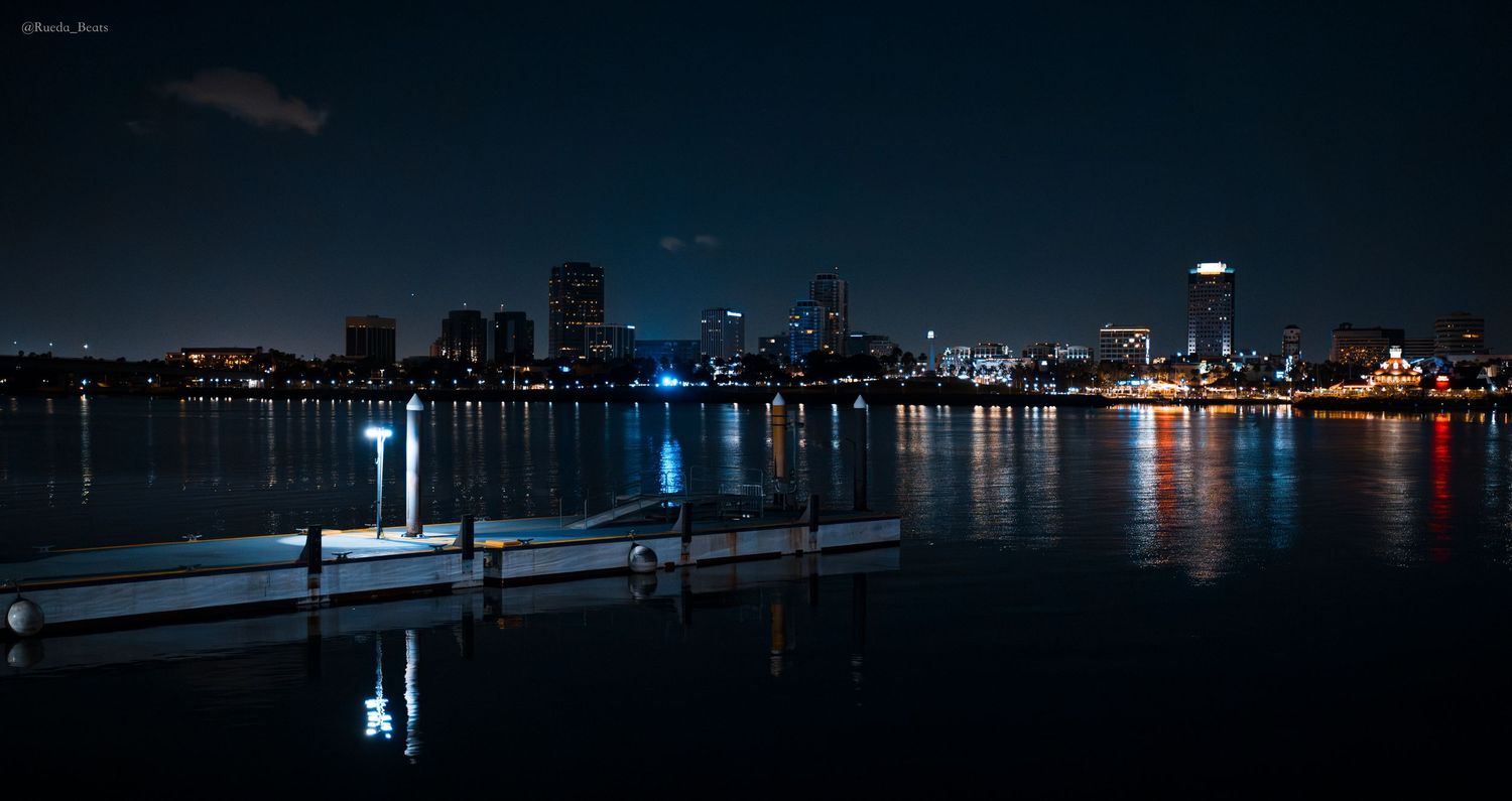 Panoramic night view of Long Beach skyline reflecting on calm harbor waters.