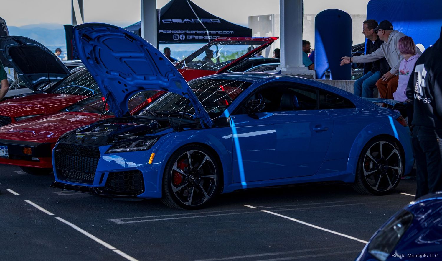 Stunning blue Audi TT RS with hood open on display at an outdoor automotive car show event.