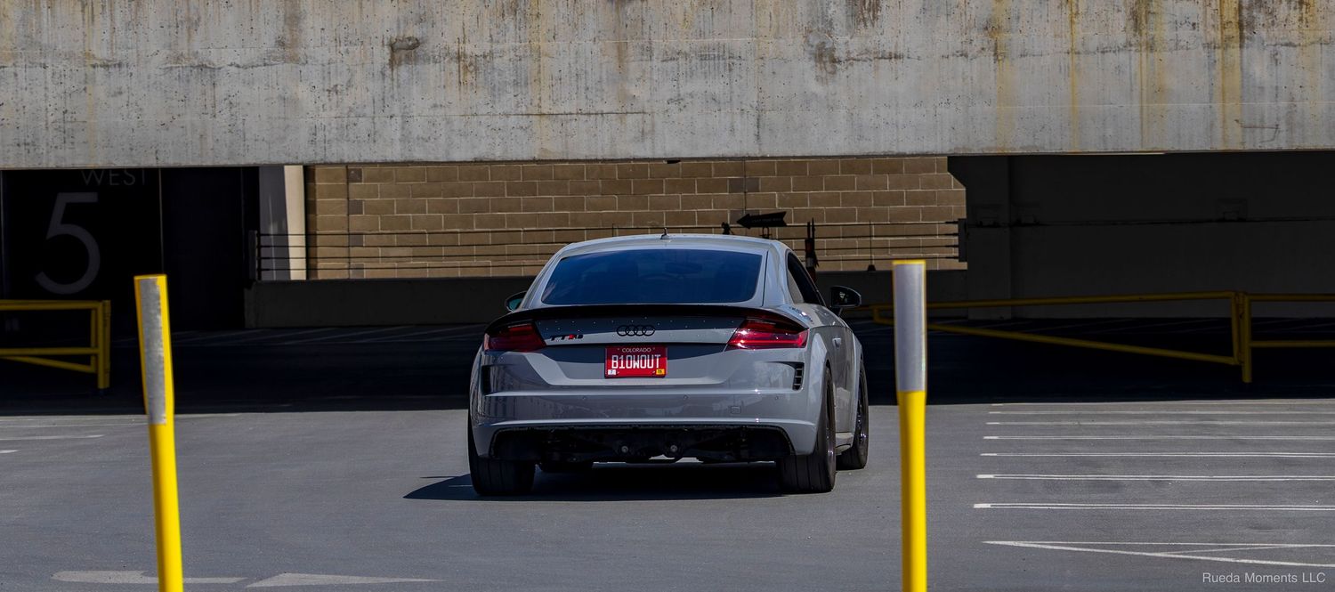 Silver Audi RS7 rear view parked between yellow bollards in a multilevel garage.