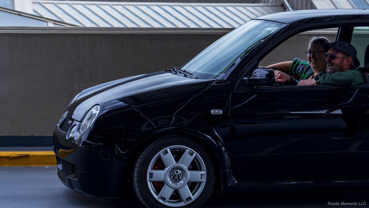Black Volkswagen Polo with occupants visible through open door in a parking structure.