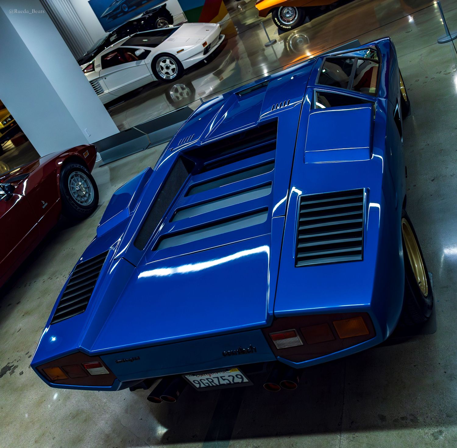 Rear view of blue Lamborghini Countach with louvered engine cover displayed in a classic car museum.