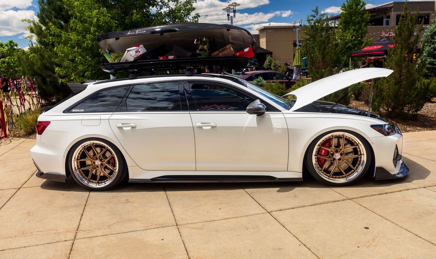 White bagged Audi RS6 Avant wagon with gold wheels and roof box at a car meet.