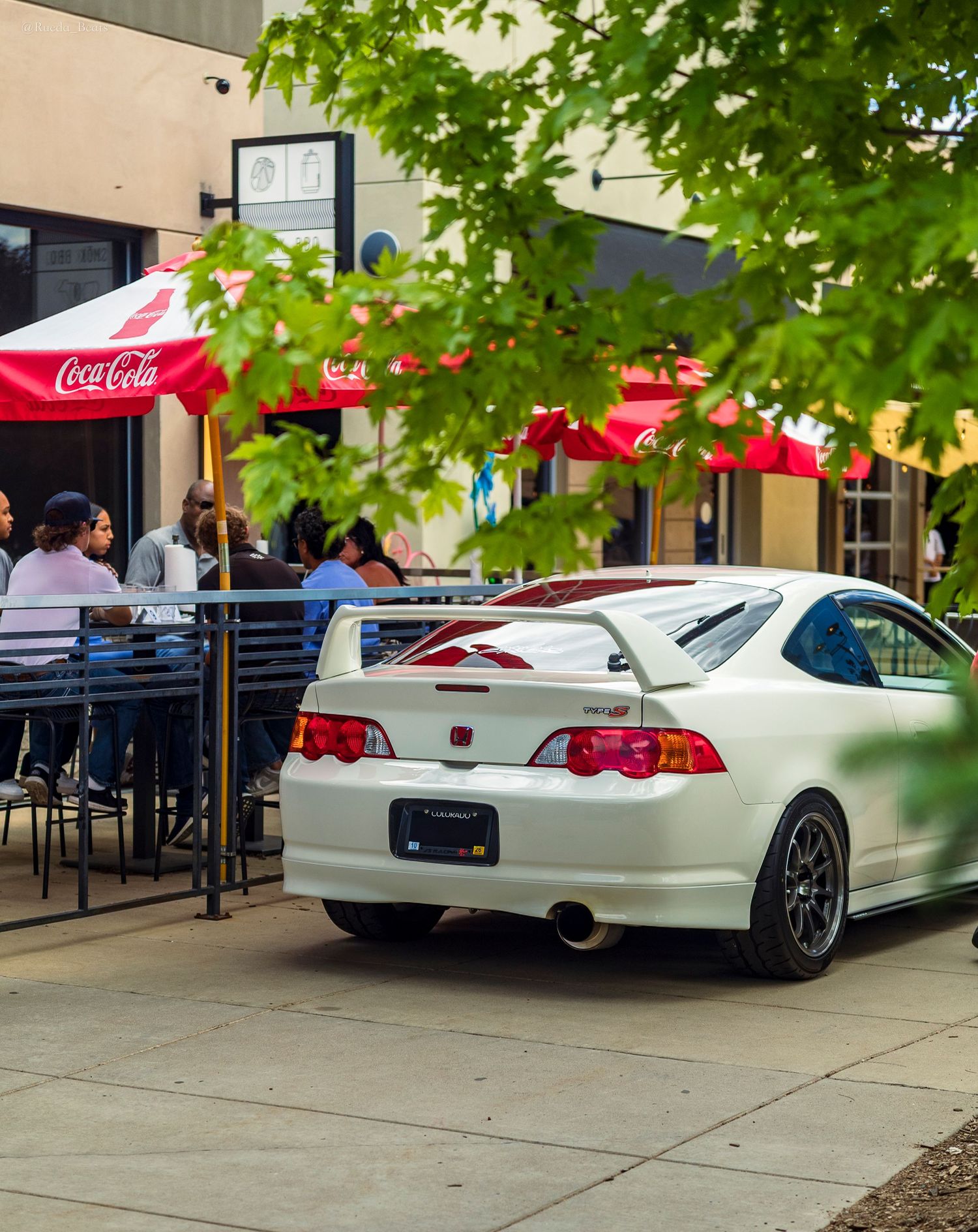 White Acura RSX Type-S coupe parked near a restaurant patio with Coca-Cola umbrellas at a car meet.