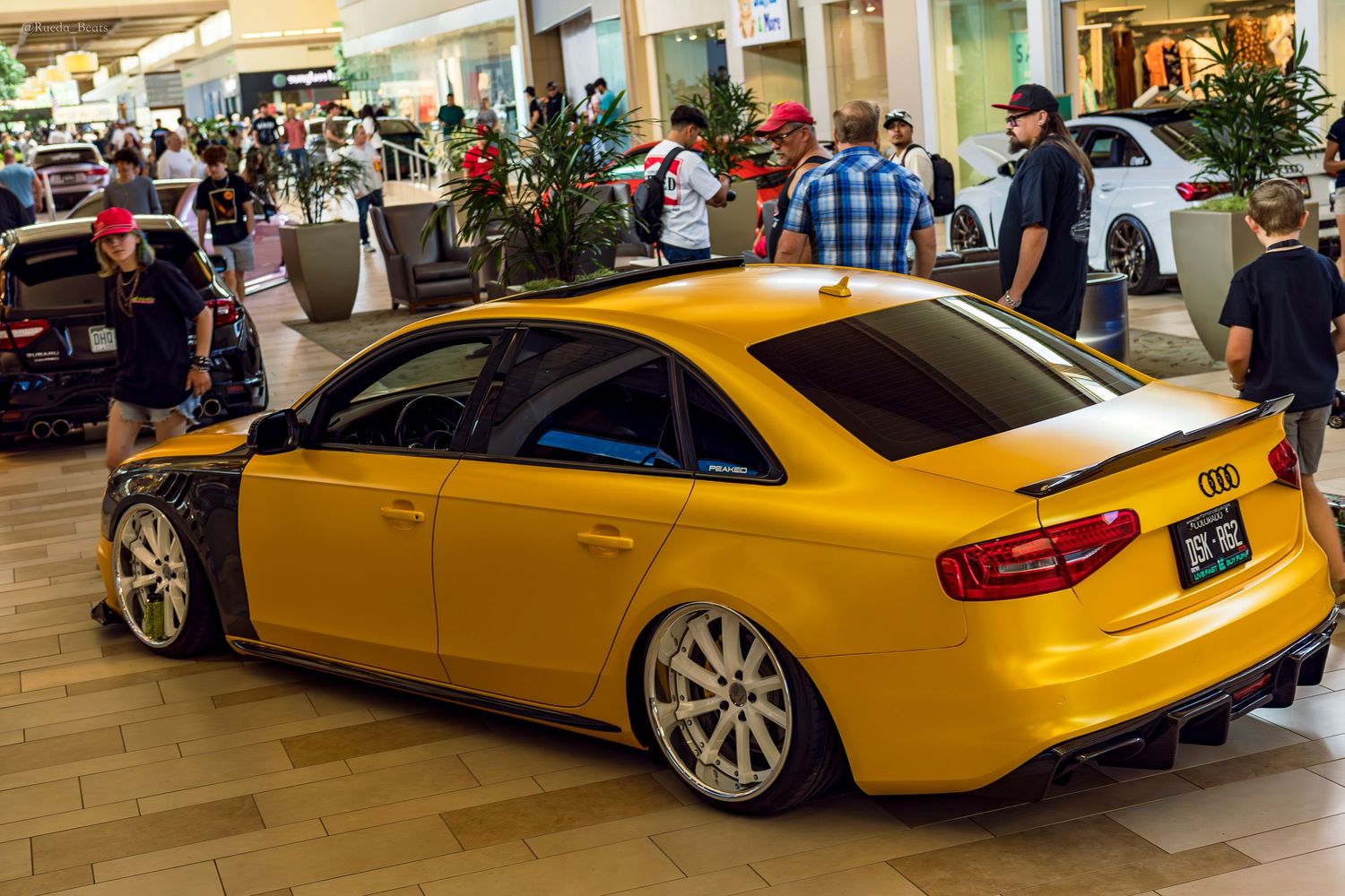 Yellow Audi RS4 widebody slammed on air suspension at an indoor car show.