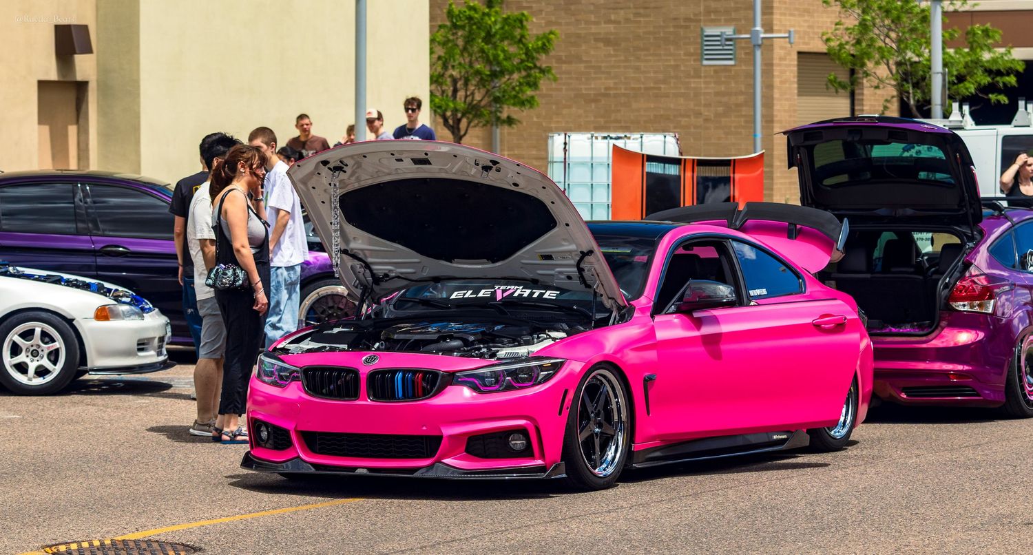 Hot pink BMW 4 Series with open hood and custom body kit at car show.