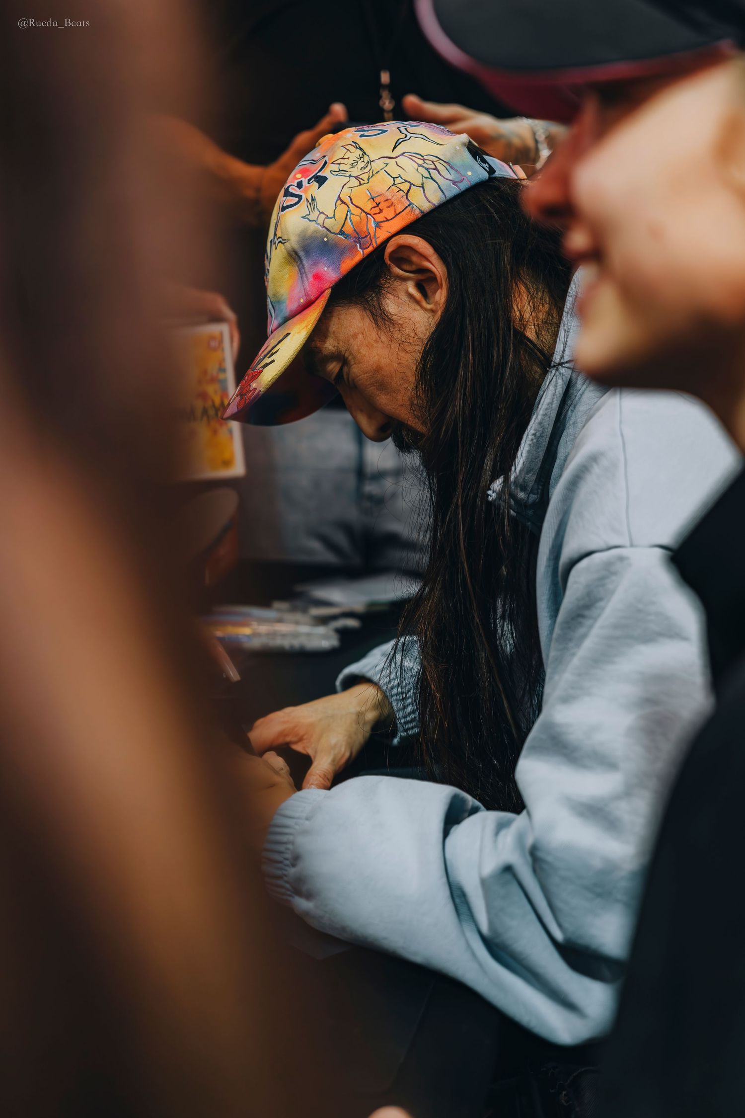 Person in colorful cap looking down while opening trading cards at an event.