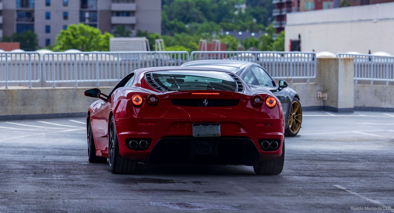 Red Ferrari F430 rear view with glowing taillights on a parking deck.