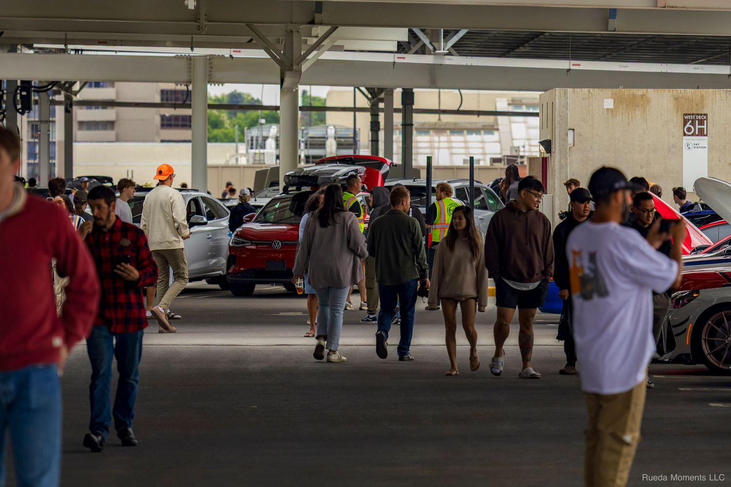 Car enthusiasts browsing modified vehicles at an indoor parking garage car show.
