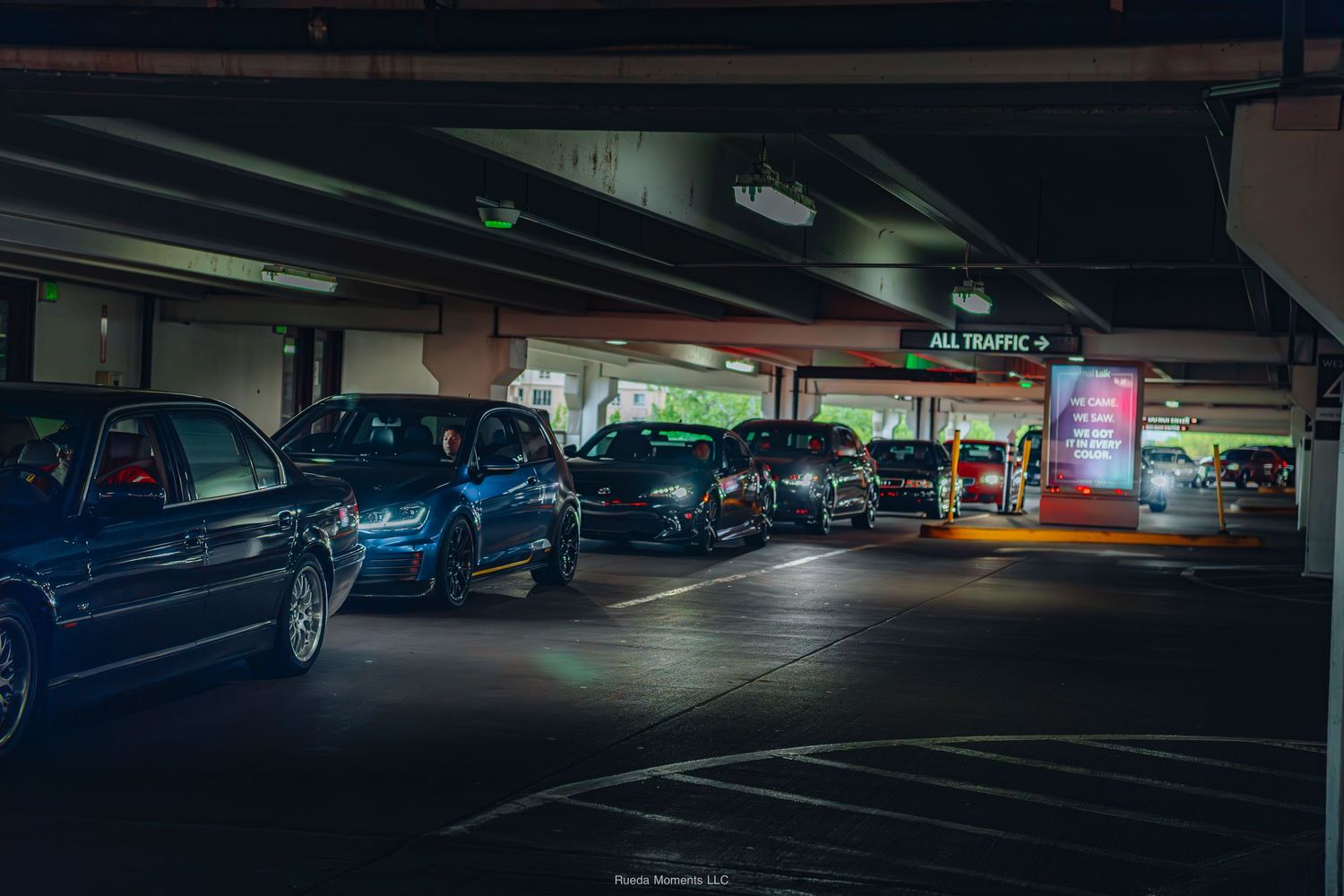 Modified luxury cars parked in a dimly lit multi-level parking garage with an All Traffic sign.