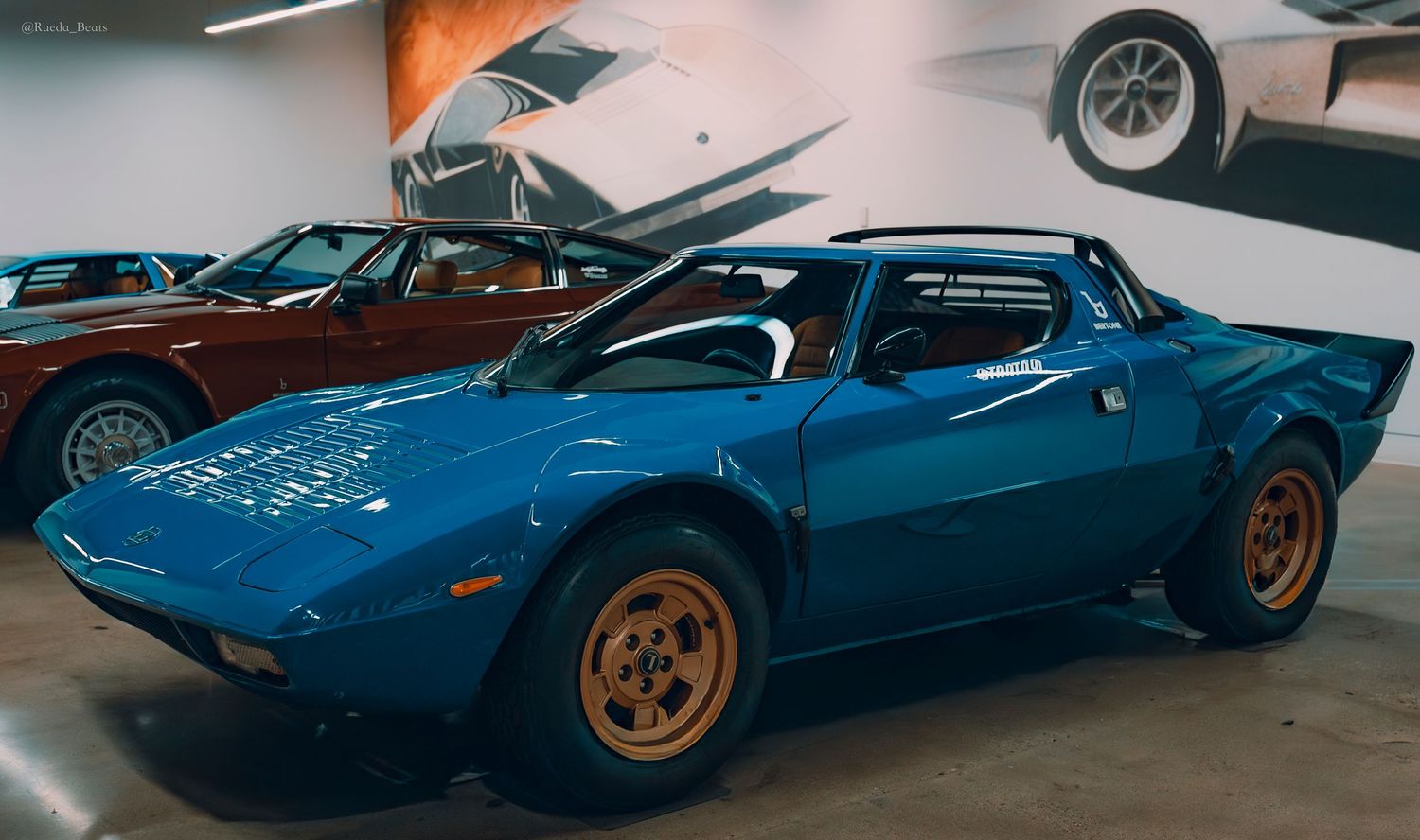 Blue Lancia Stratos classic Italian sports car with gold wheels displayed in an automotive museum.