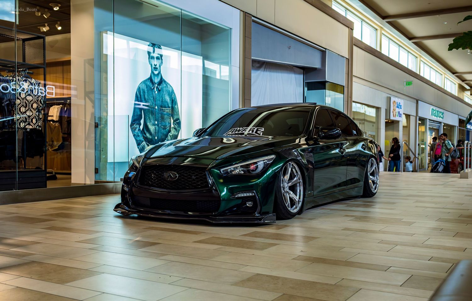 A lowered dark green Infiniti Q50 with custom aero kit on display inside a shopping mall.