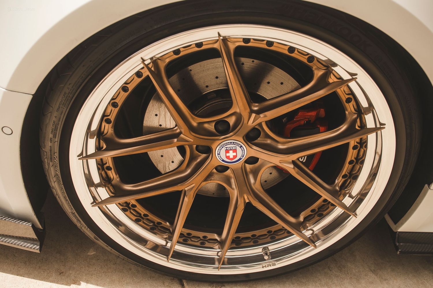 Gold HRE forged split spoke wheel with red brake caliper on a white sports car.