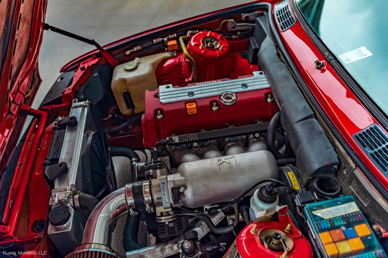Red car engine bay showcasing a clean performance build with red valve cover and intake components.