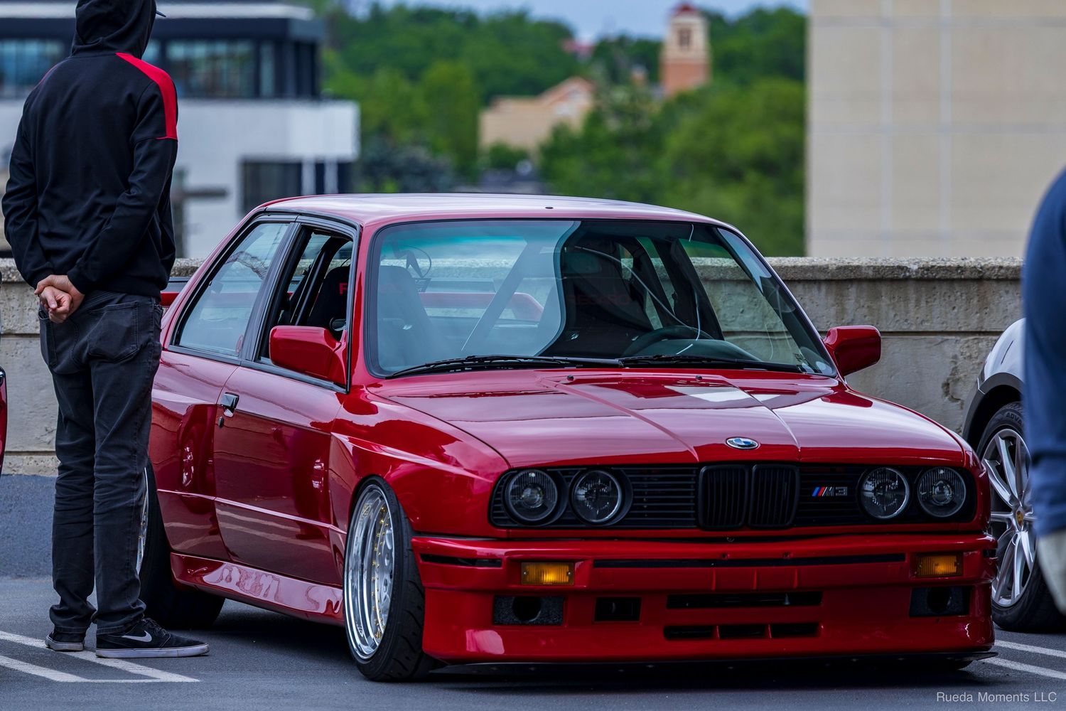 Red BMW E30 M3 on silver mesh wheels parked at an outdoor car meet.