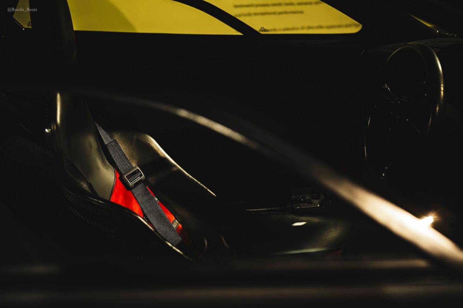 Dark interior view of a sports car showing racing harness seat belts and bucket seat detail.
