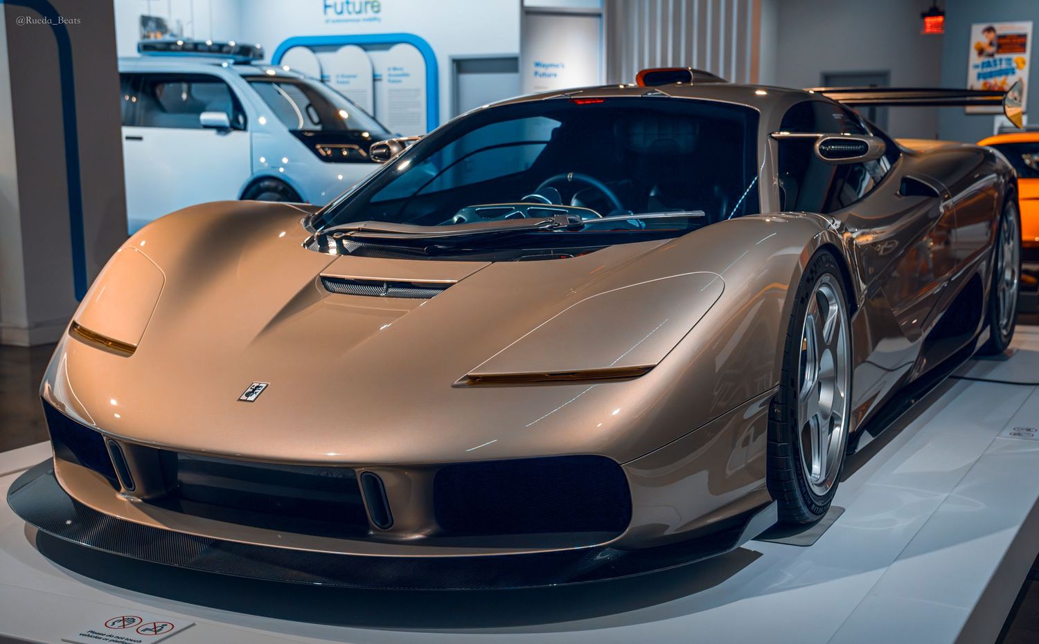 Sleek bronze-colored supercar on display at a modern automotive museum exhibit.