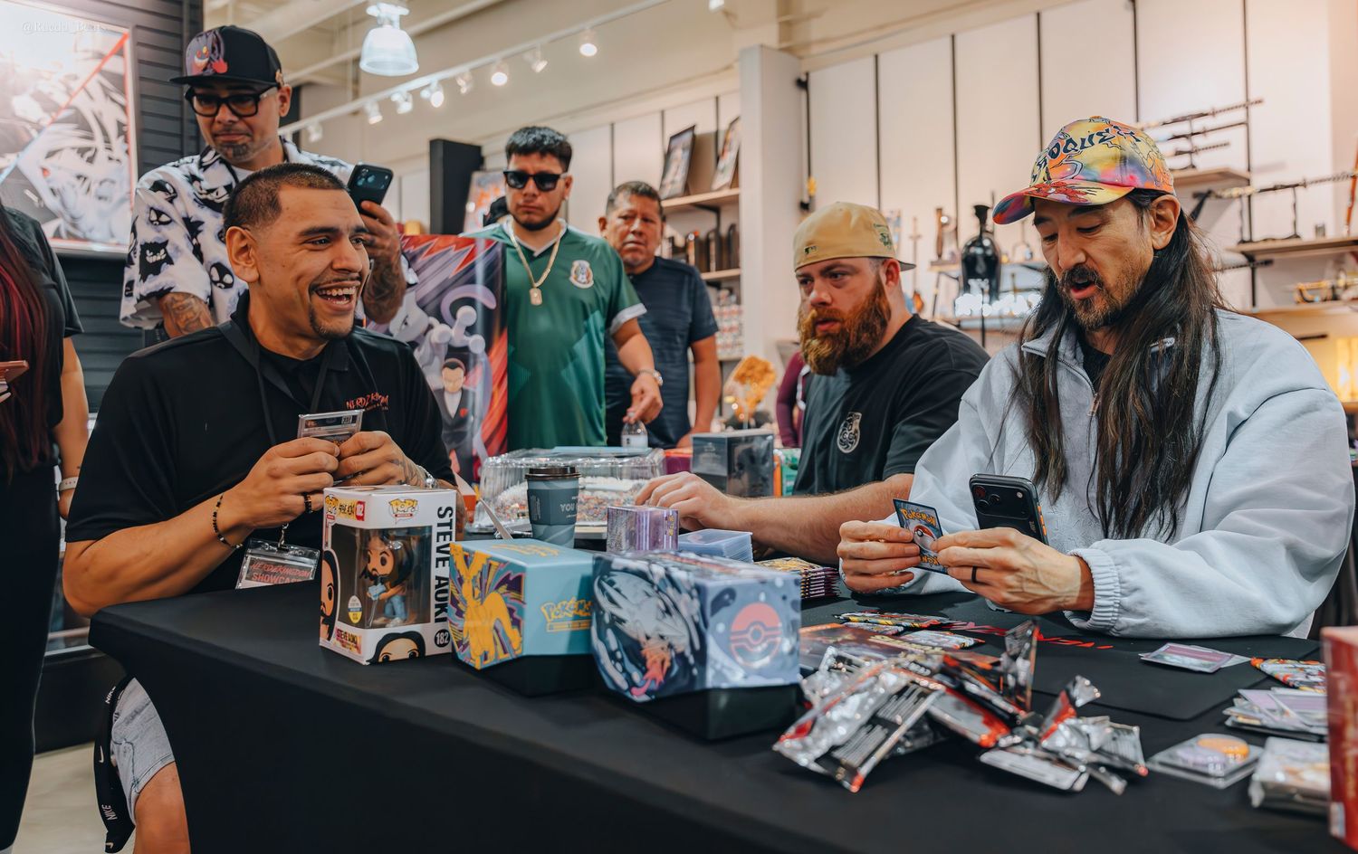 Three men laughing and opening trading card packs together at a retail store event.