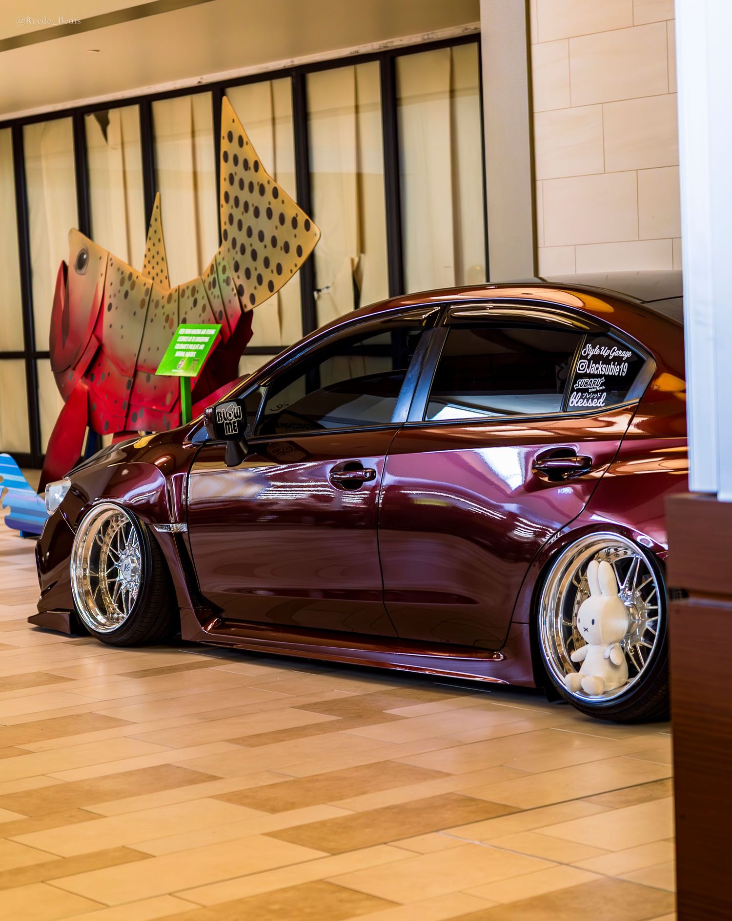 Maroon Toyota Prius widebody slammed on chrome mesh wheels at indoor car show.