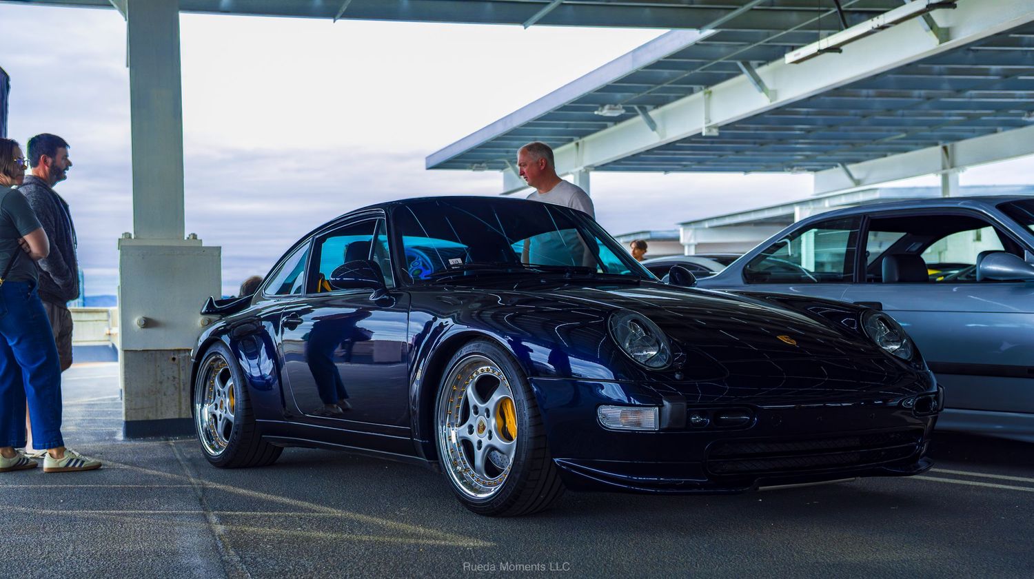 Dark blue Porsche 993 911 with chrome wheels at an outdoor car meet.