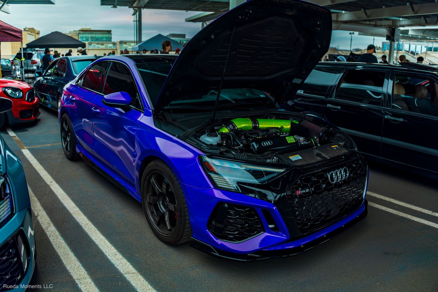 Blue Audi RS with hood open revealing a neon green engine bay at a car show event.
