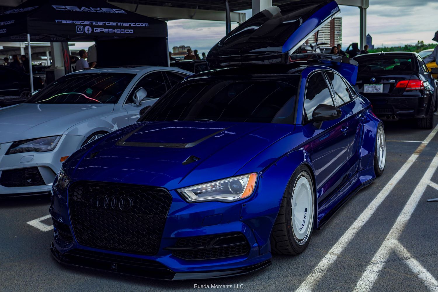 Widebody blue Audi RS3 with hood open displayed at car show.