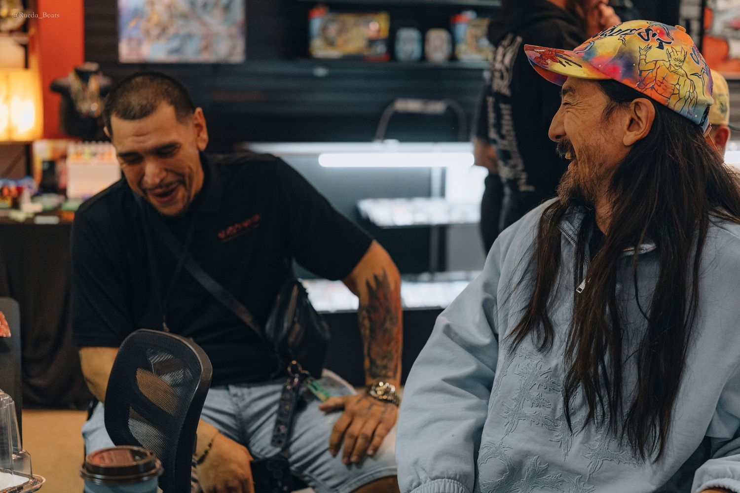 Two men laughing together in a tattoo shop setting.