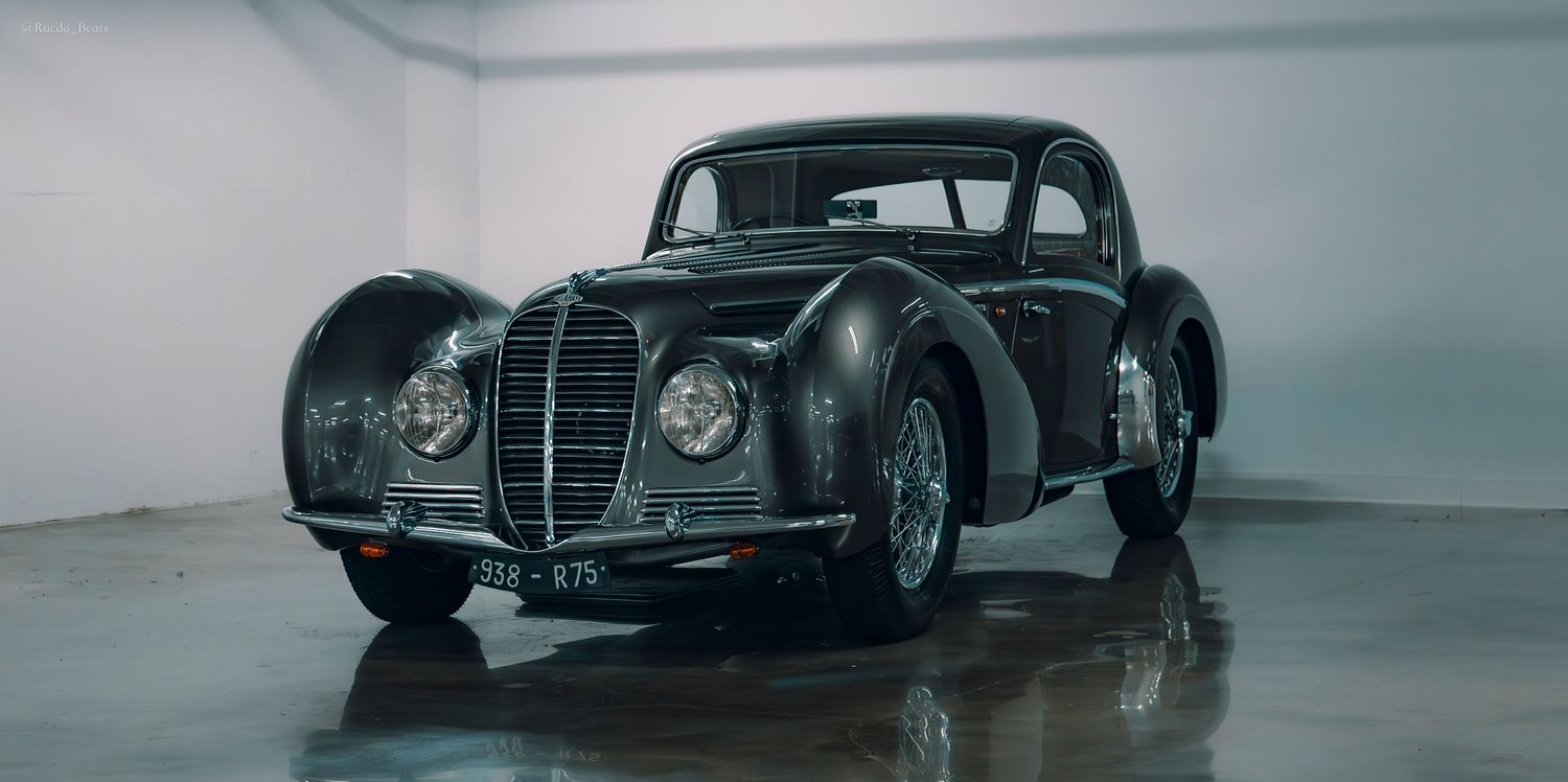 Vintage black pre-war coupe car displayed in a white studio, showcasing classic 1940s aerodynamic design.