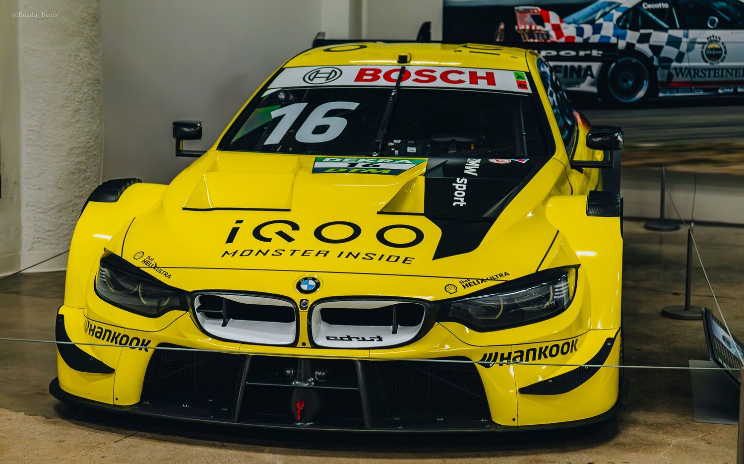 Yellow BMW M4 DTM race car number 16 with iQOO and Hankook sponsorship on display.